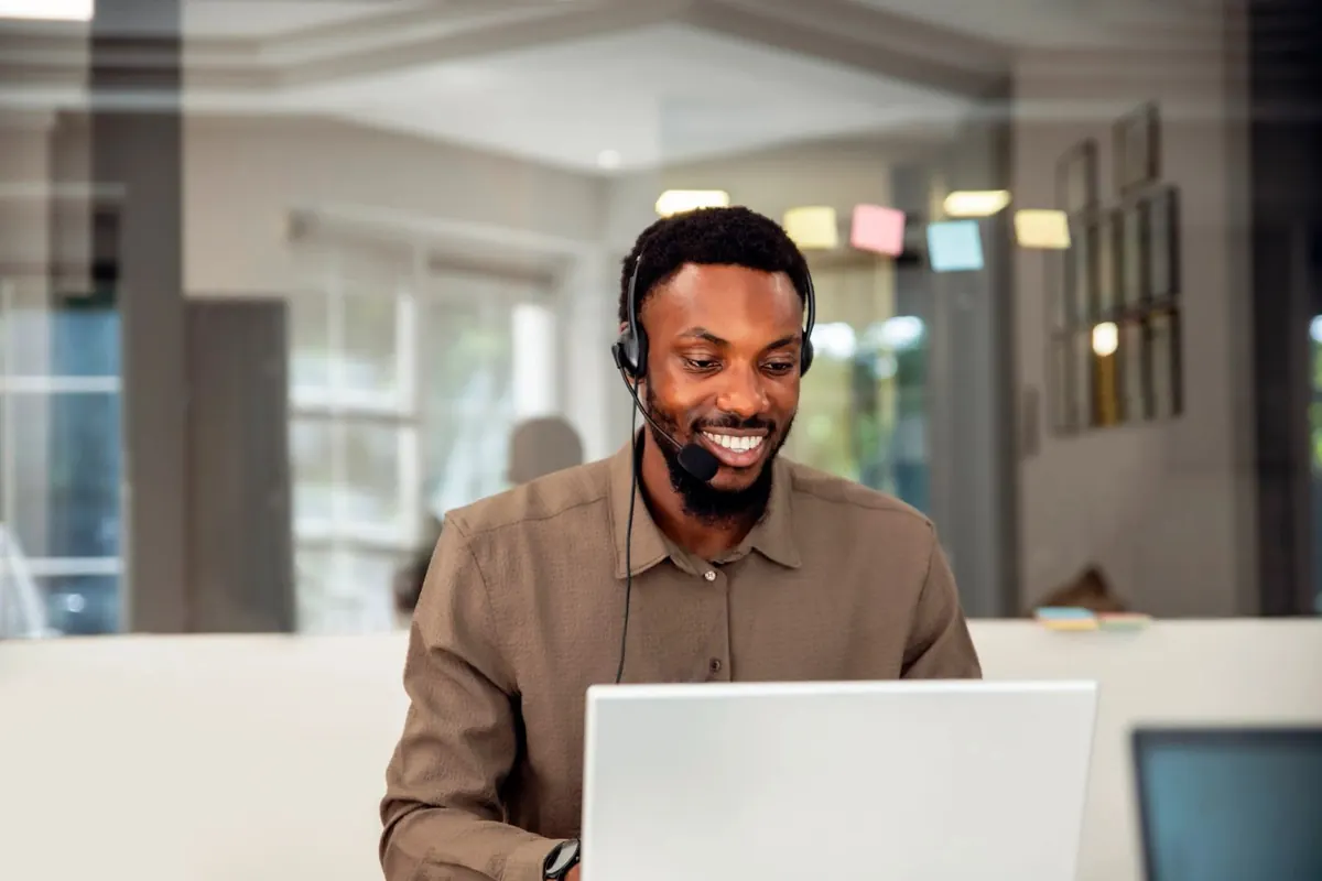 Smiling customer service agent with a headset working at a laptop