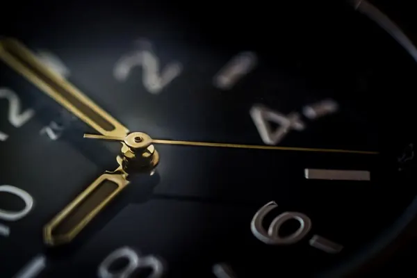 Close-up of a clock face with golden hands on a dark background.