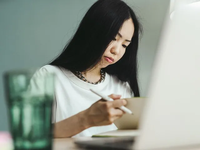 Woman writing in a notebook beside a laptop.